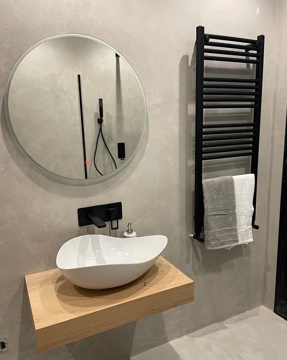 Baño microcemento · Grifo negro empotrado · Espejo redondo · Toallero calefactor