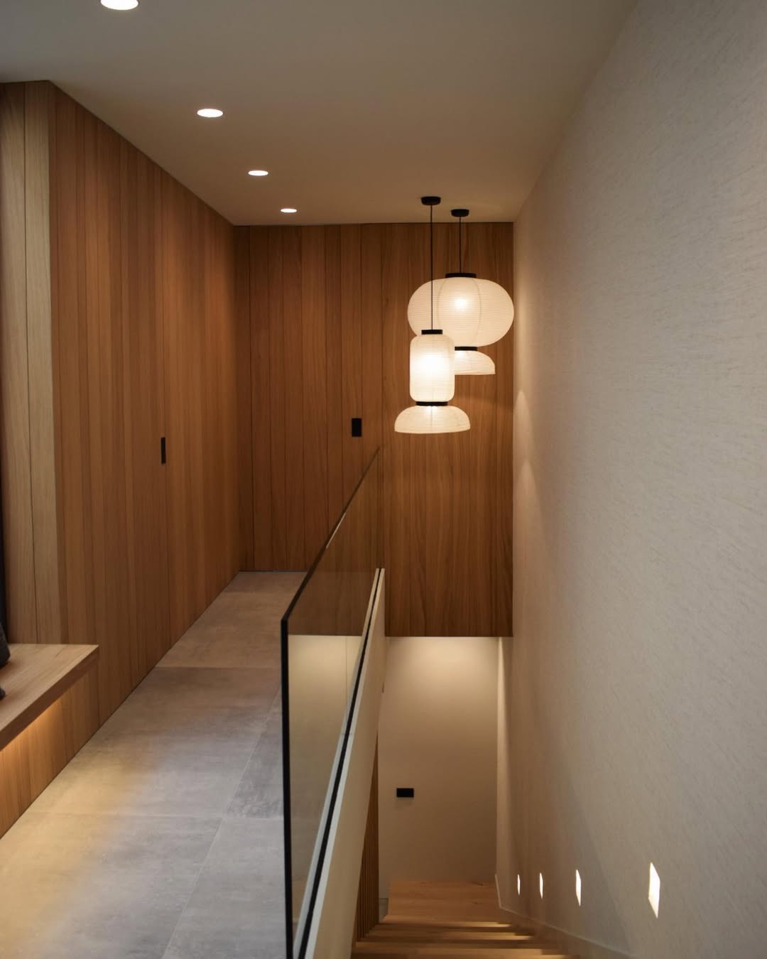 Corredor con revestimiento de madera · Lámparas globo colgantes · Iluminación cálida